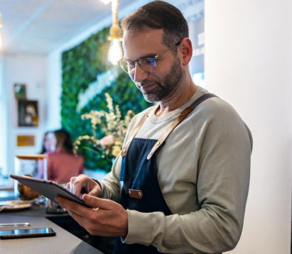 Man in coffee shop holding a tablet smiling