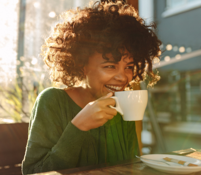 Woman drinking a cup of coffee smiling and wearing a green jumper